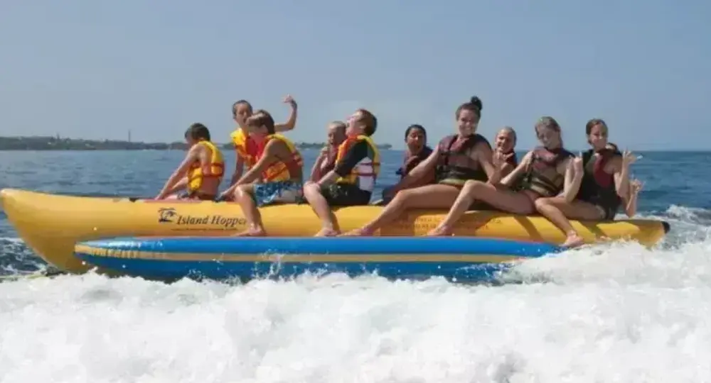 group of people riding a yellow banana boat in the ocean with life jackets