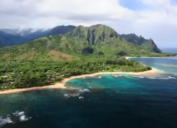 tropical coastline with sandy beach, turquoise waters, and lush green mountains under partly cloudy sky