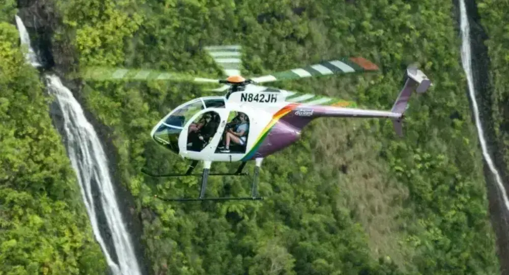 helicopter flying near waterfalls over green forested hills