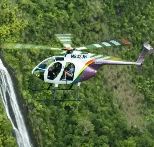 helicopter flying near waterfalls over green forested hills