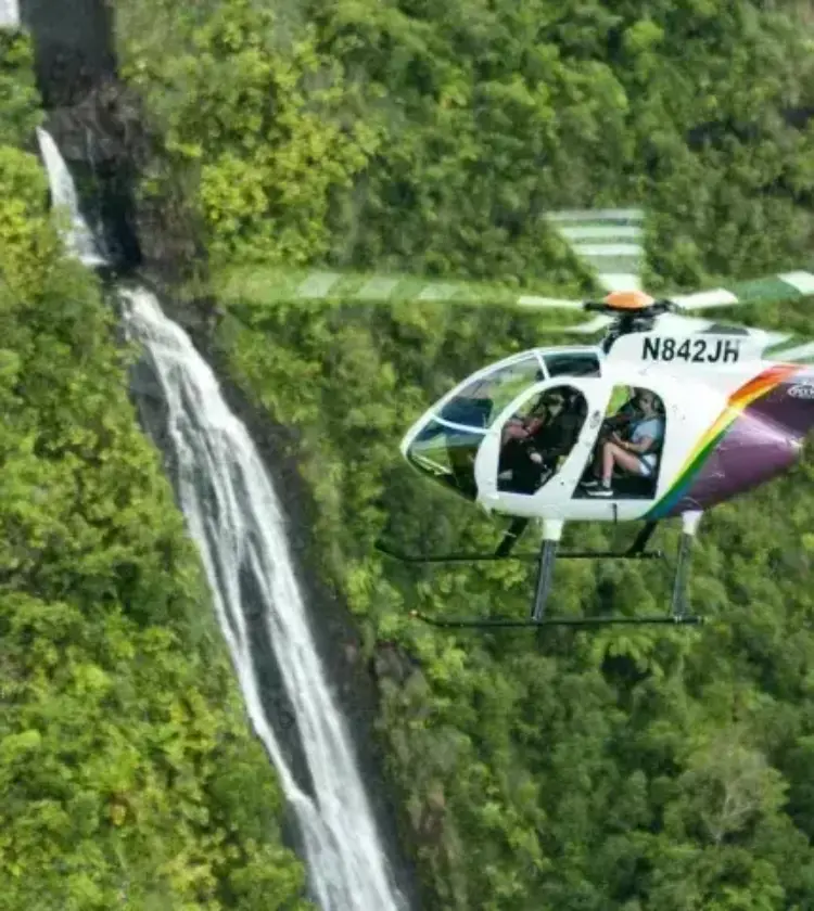 helicopter flying near waterfalls over green forested hills