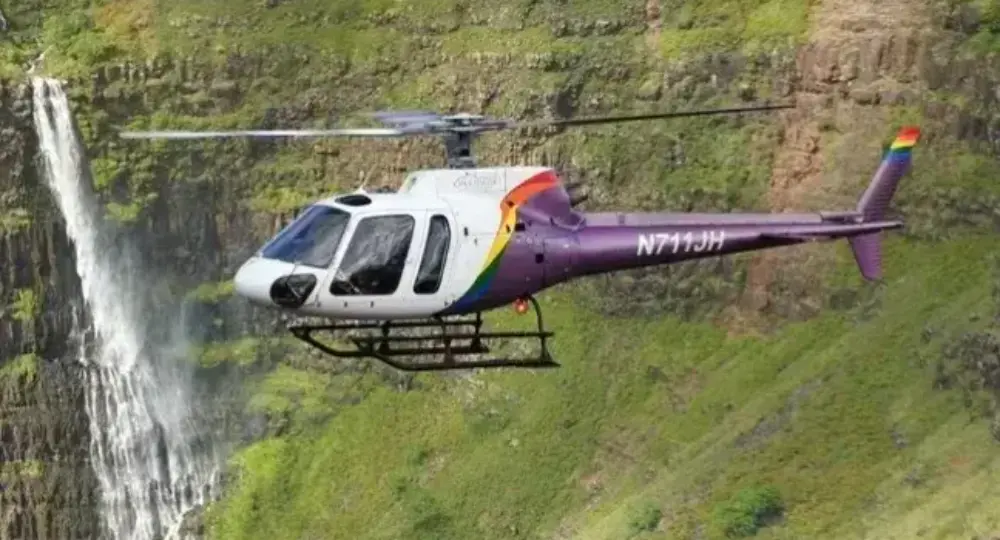 Helicopter flying near waterfall and green cliffs in Hawaii