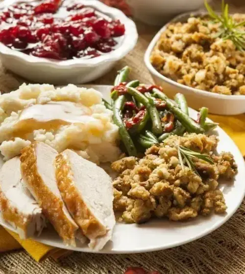Plate with sliced turkey, mashed potatoes, green beans, stuffing and bowls of cranberry sauce, corn, and other side dishes
