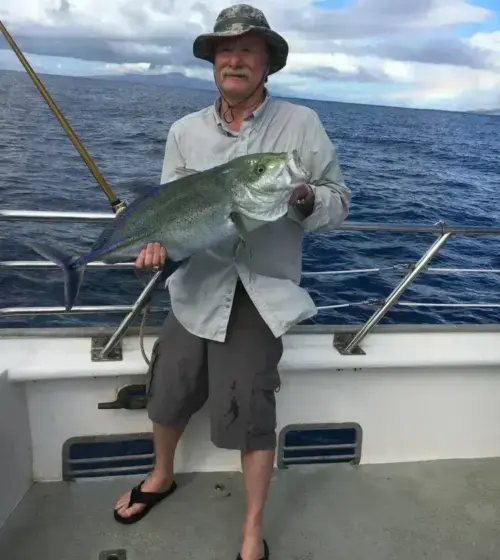 man wearing hat and shorts holding large fish on fishing boat with ocean background