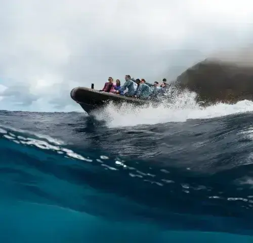 Group of people riding an inflatable boat on ocean waves near volcanic cliffs