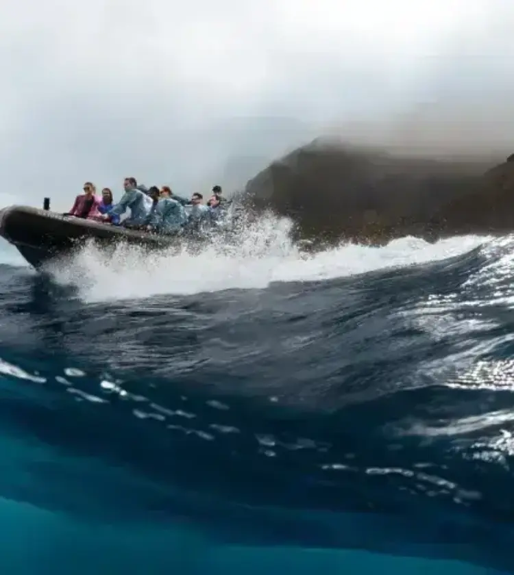 Group of people riding an inflatable boat on ocean waves near volcanic cliffs