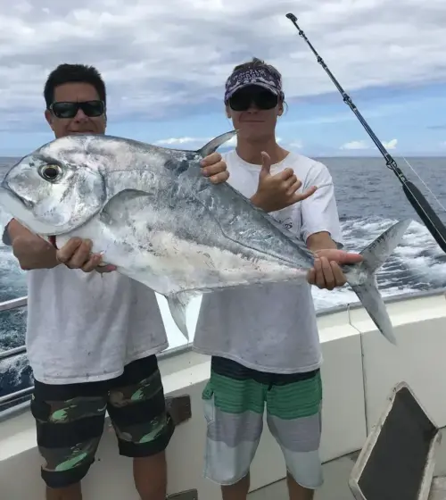 two men on boat holding a large silver fish with ocean in background