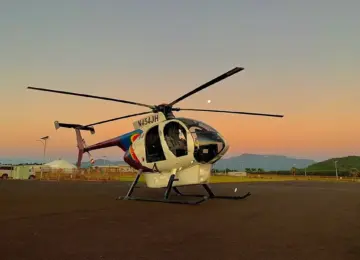 Helicopter parked on airfield during sunset with hills in background