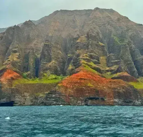 Steep Na Pali Coast cliffs with green and red vegetation rising from blue ocean