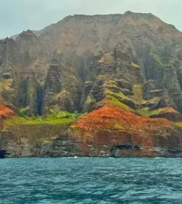 Steep Na Pali Coast cliffs with green and red vegetation rising from blue ocean