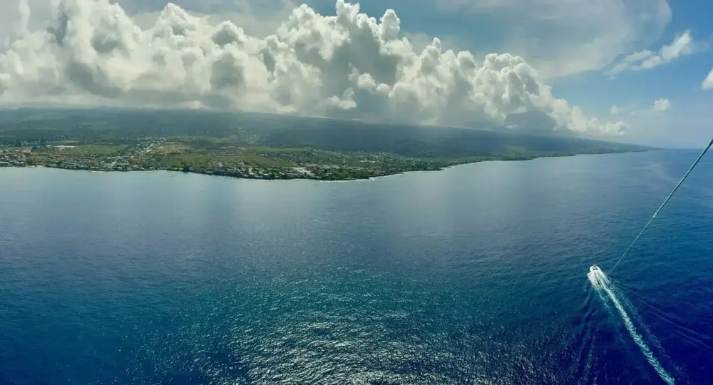 Aerial view of coastline under cloudy sky with a small boat on blue ocean
