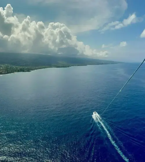 Aerial view of coastline under cloudy sky with a small boat on blue ocean