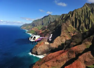 Helicopter flying along the Na Pali Coast with towering cliffs and blue ocean