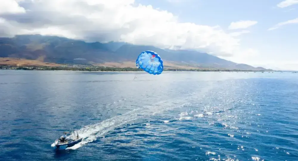 Boat towing a blue parasail over ocean with mountainous coastline in background