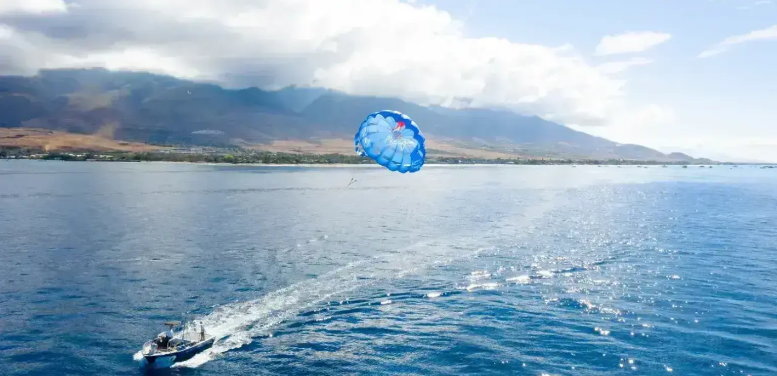 Boat towing a blue parasail over ocean with mountainous coastline in background