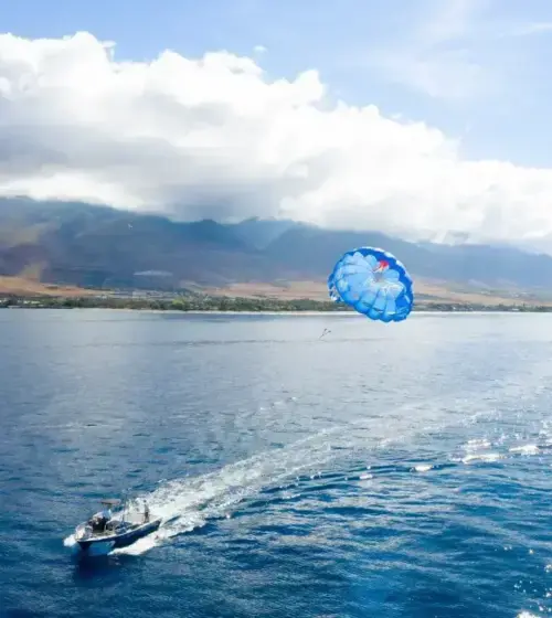 Boat towing a blue parasail over ocean with mountainous coastline in background