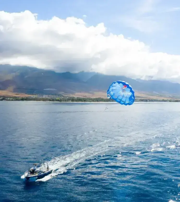 Boat towing a blue parasail over ocean with mountainous coastline in background