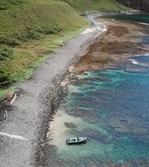 Boat anchored near rocky coastline with clear turquoise water and coral reef