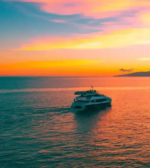 Tour boat sailing on calm ocean at colorful sunset with island silhouette in background