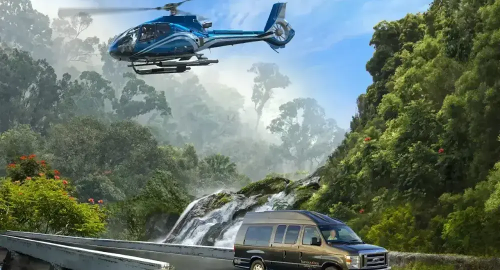 Blue helicopter flying over lush green mountains and a tour van driving on a curved bridge near a waterfall