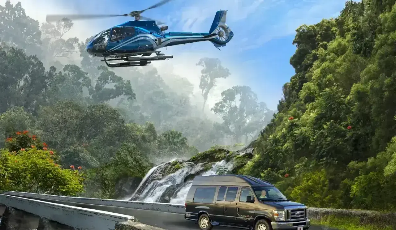 Blue helicopter flying over lush green mountains and a tour van driving on a curved bridge near a waterfall