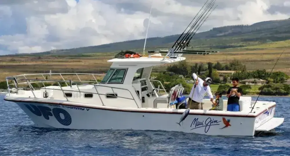 Fishing boat with people fishing on ocean near shore with hills