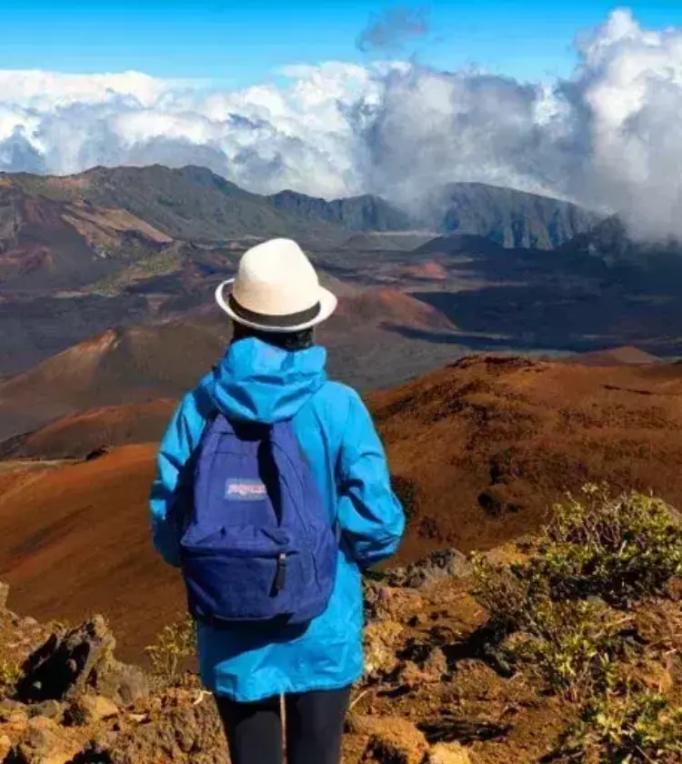 hiker in blue jacket and white hat looking over volcanic landscape