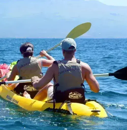 two people kayaking on a yellow kayak in the ocean with mountains in background