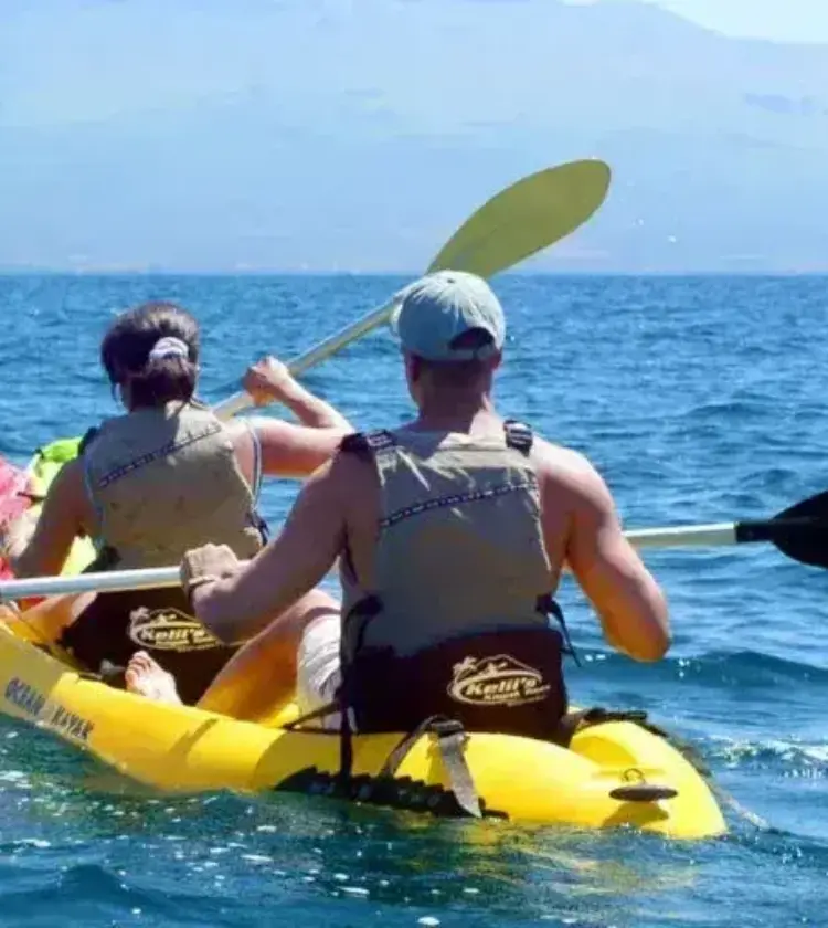 two people kayaking on a yellow kayak in the ocean with mountains in background