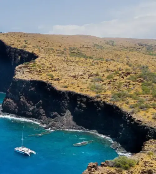 coastal cliffs with a sailboat anchored in turquoise waters