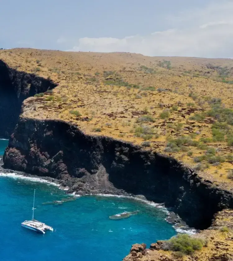 coastal cliffs with a sailboat anchored in turquoise waters