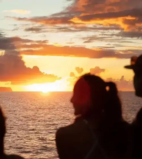 silhouetted people watching sunset over ocean with colorful sky