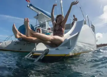 woman sliding joyfully into ocean from a white sailboat on sunny day