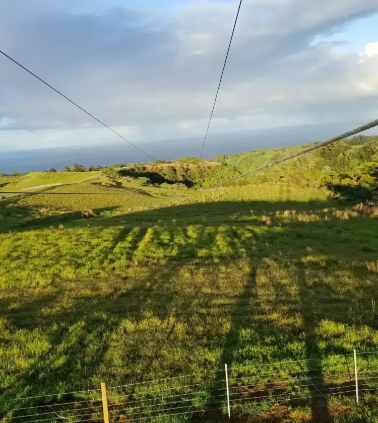 zip line cables extending over green rolling hills toward ocean under partly cloudy sky
