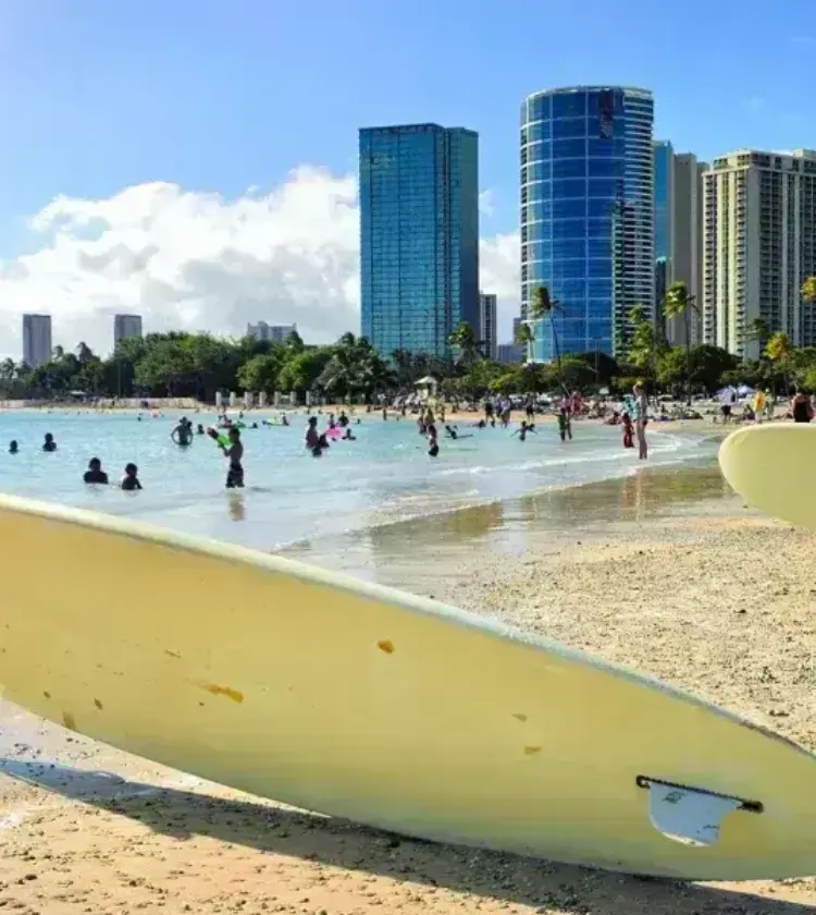 Two surfboards standing upright on sandy Waikiki beach with people swimming and city skyscrapers in background