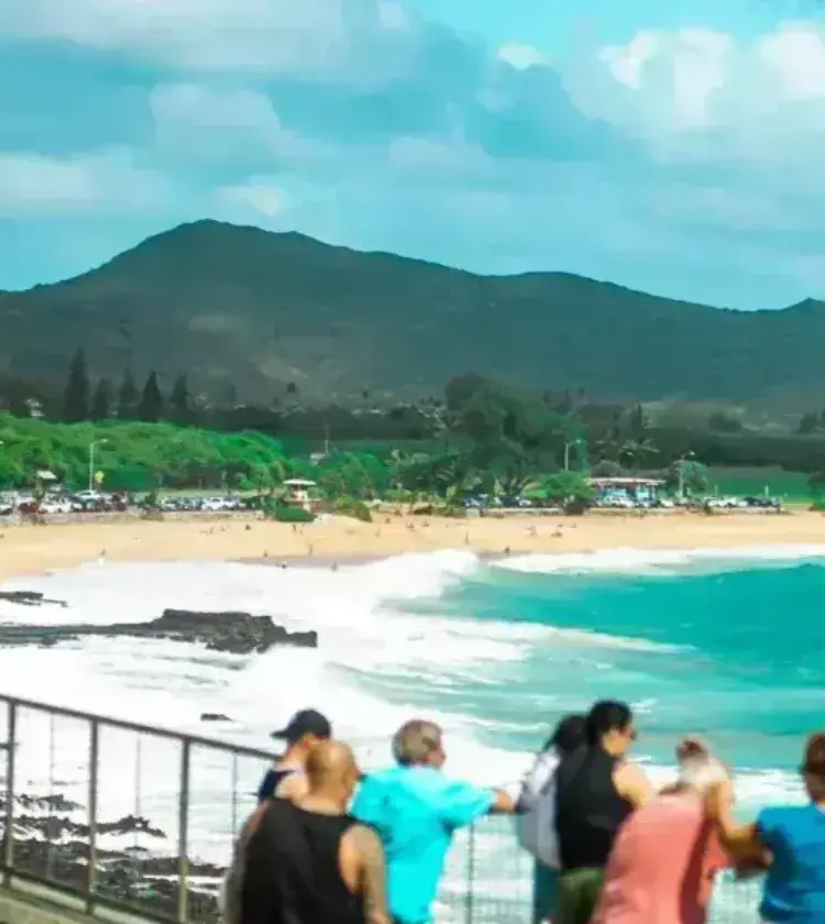 People viewing a Hawaiian beach with turquoise ocean and lush mountains in the background