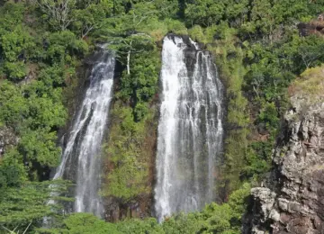 Twin waterfalls flowing down lush green tropical cliffs with surrounding dense vegetation and rocky outcrops