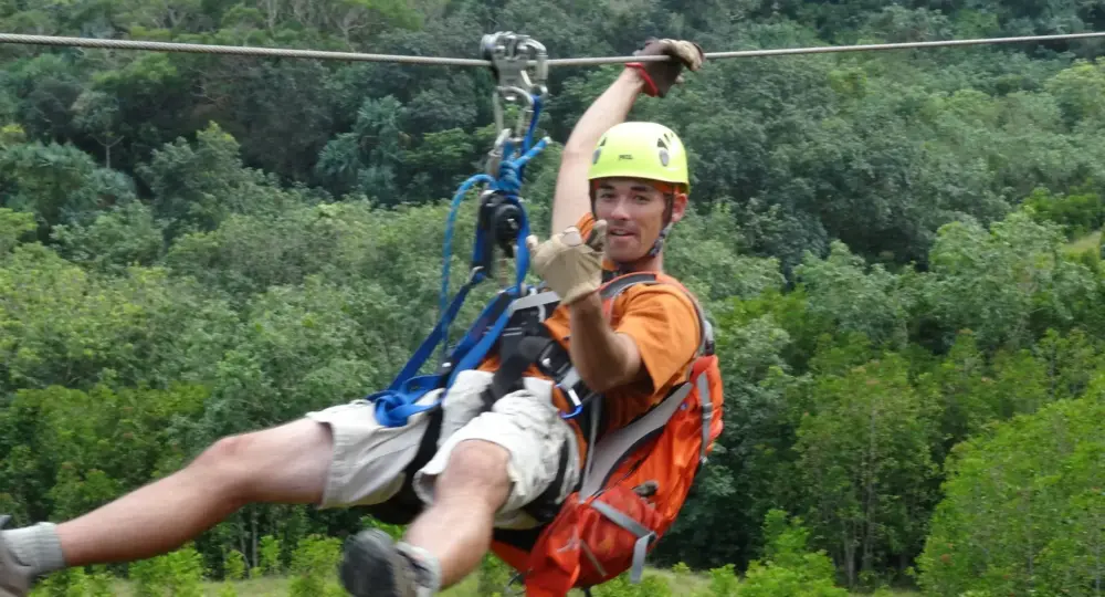 man ziplining in forest wearing yellow helmet orange backpack