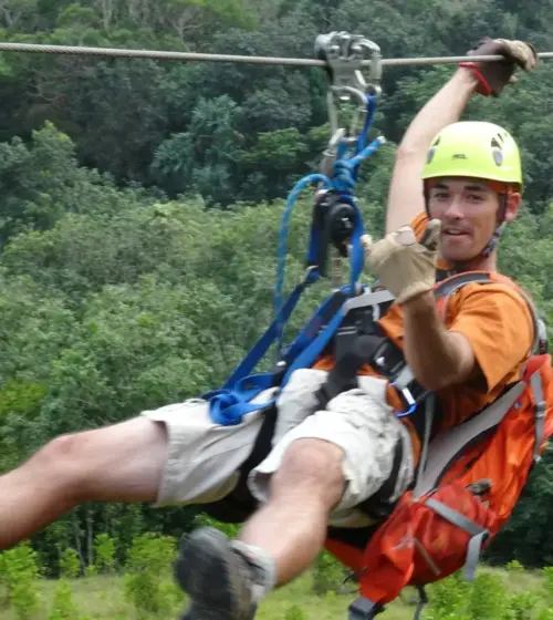 man ziplining in forest wearing yellow helmet orange backpack