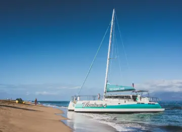 catamaran boat named Teralani 4 near sandy beach with few people and ocean under clear blue sky