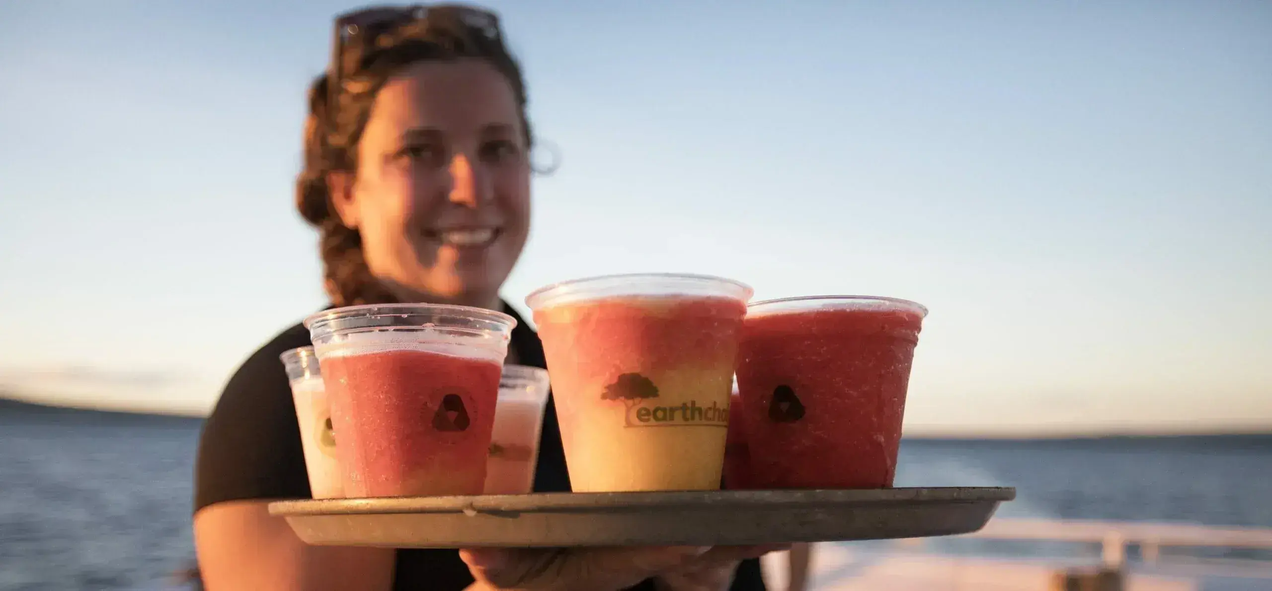 tropical layered fruit drinks on tray held by woman by ocean