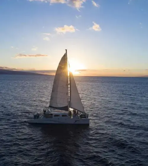 Sailboat sailing on ocean at sunset with island silhouette in background