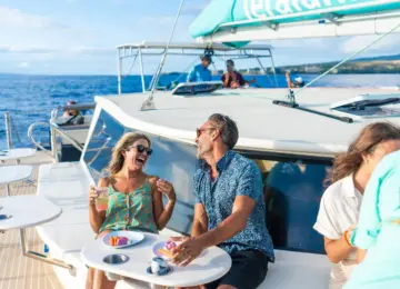 Man and woman laughing and enjoying drinks on boat deck with ocean background
