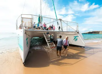 people disembarking large catamaran on sandy beach with blue sky