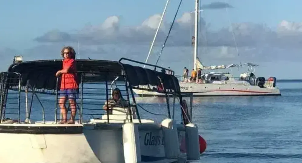 Two boats on calm ocean water with people on deck under partly cloudy sky