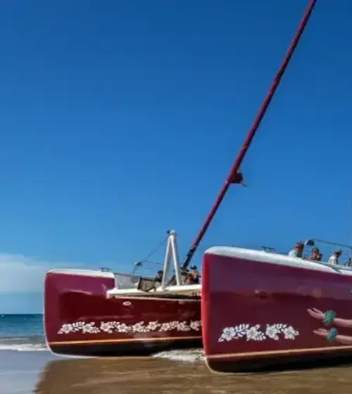red catamaran sailboat on sandy beach with calm sea and passengers