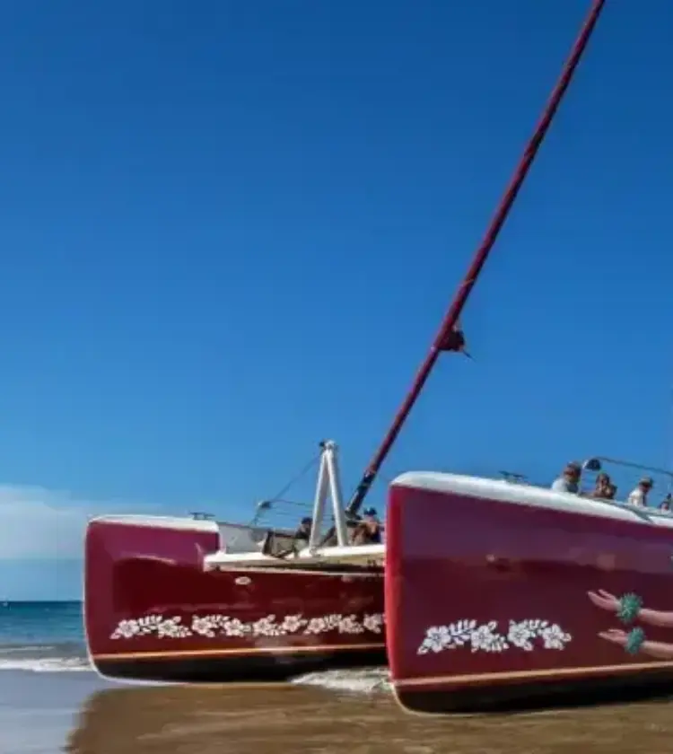 red catamaran sailboat on sandy beach with calm sea and passengers