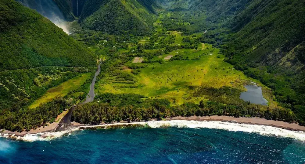 lush green Hawaiian valley with coastline, river, and waterfall