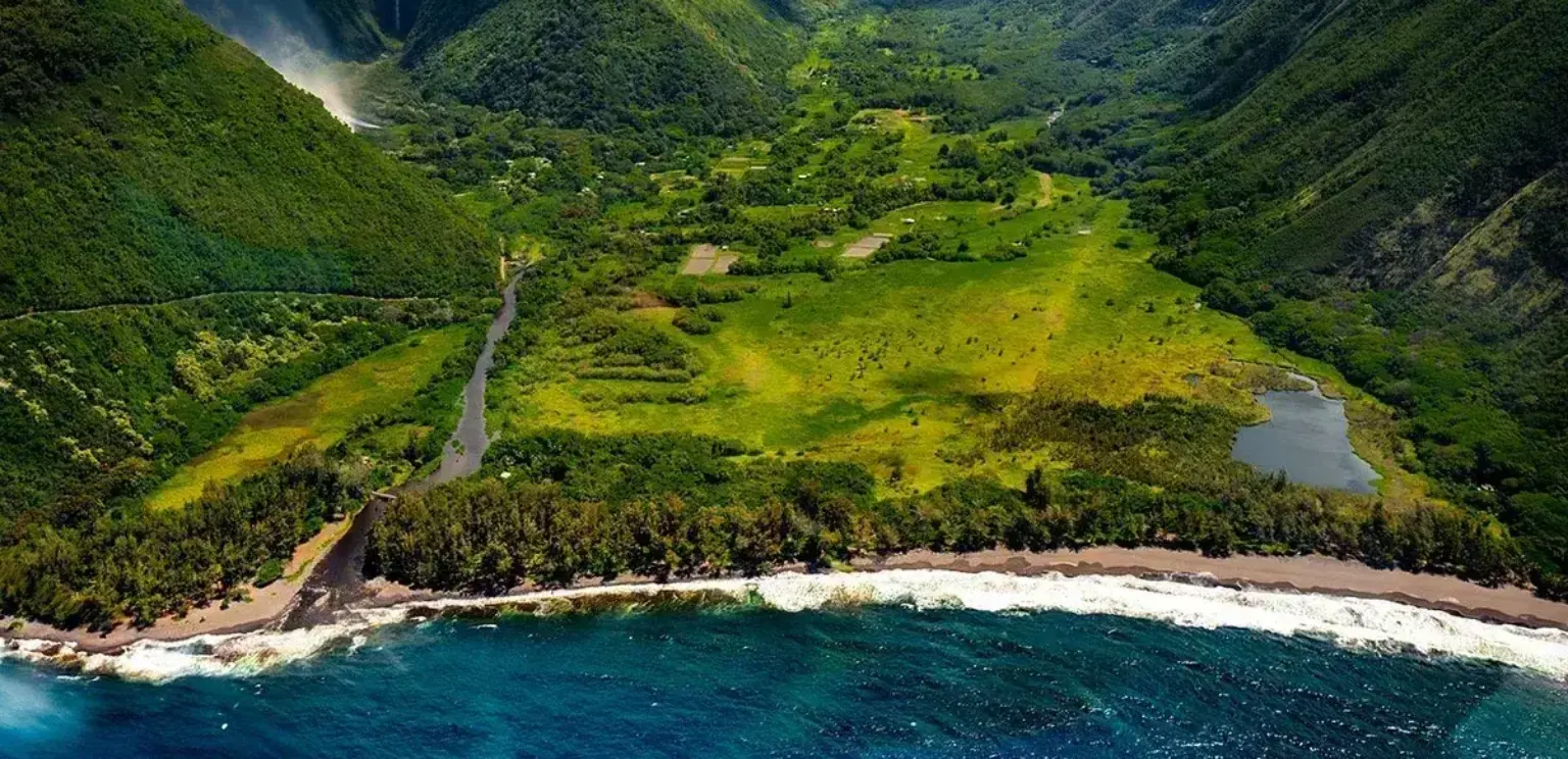 lush green Hawaiian valley with coastline, river, and waterfall