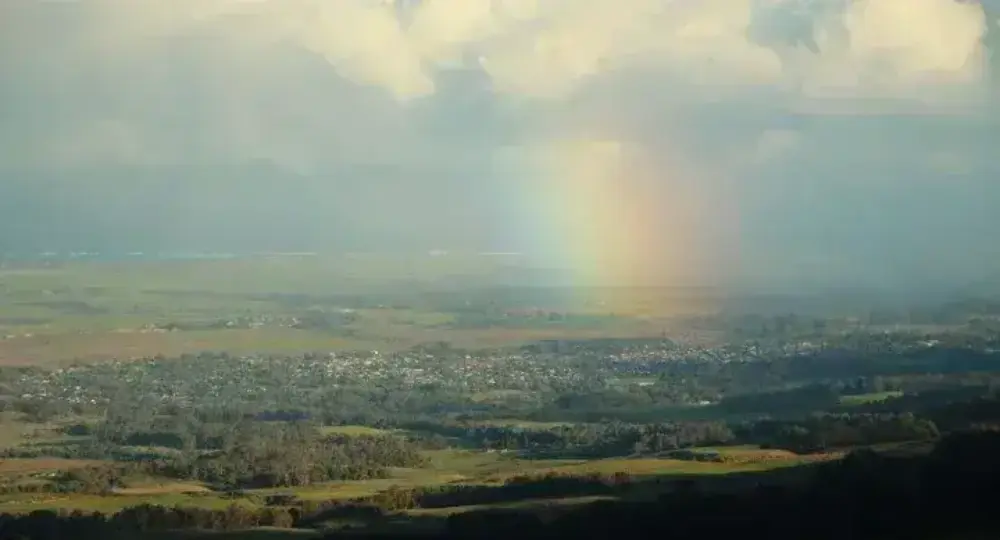 Rainbow appearing over a rural landscape with scattered clouds